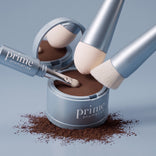 An open blue container of PrimePrometics™ 4-in-1 Hairline Powder Brush sits against a light blue background, with powder scattered beneath it. Three makeup brushes—including the versatile 4-in-1 applicator—rest on and inside the container. Each brush features soft, cruelty-free bristles to ensure flawless application every time.