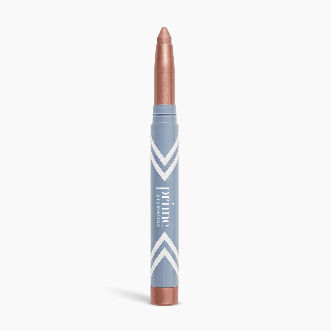 A metallic rose gold illuminating eyeshadow stick, the PrimeEyes Eye Brightener by PrimePrometics™, stands upright against a white background in its sleek blue and white tube—perfect for creating an effortless eye lift effect.
