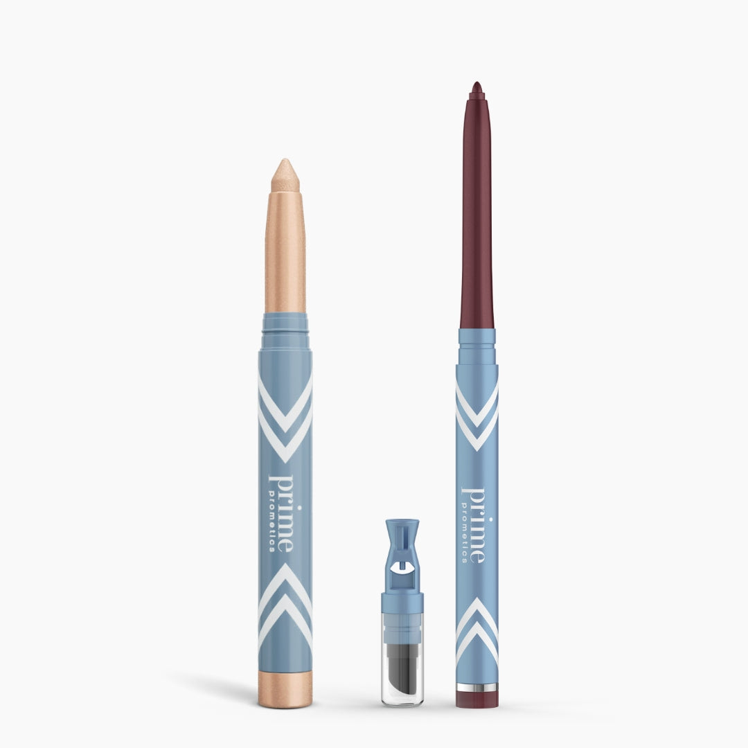 Two blue Eye Lift Duo makeup pencils by PrimePrometics™ stand upright—one with a beige tip, one with a dark brown tip—ideal eyeliner for women over 50. A small sharpener with a clear cap sits between them; all feature white chevrons and branding.