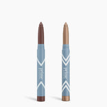 Two blue PrimePrometics™ Complete Eye Sticks stand upright on a white background: the left has a brown tip and base, the right has a light bronze tip. Both provide matte eyeshadow shades to brighten your eyes.