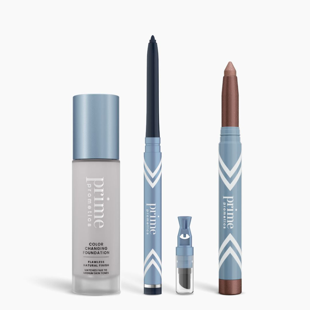 The PrimePrometics™ All-Day Confidence Bundle includes four makeup items with light blue and silver packaging—color-changing foundation, glide eyeliner pencil, replaceable eyeshadow cartridge, and chubby eyeshadow stick—standing upright on a white background.