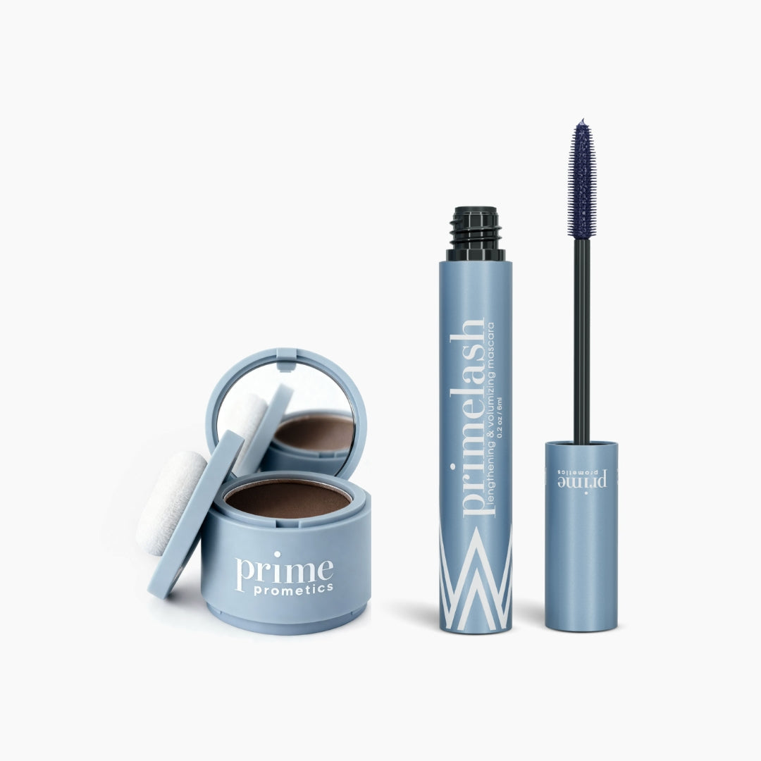 The PrimePrometics™ Beauty Essentials set features two blue products: a mirrored round hairline powder compact with puff and an open PrimeLash mascara tube with exposed wand.