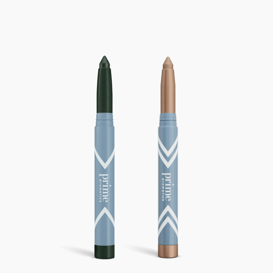 The PrimePrometics™ Complete Eye Sticks Kit, featuring blue and white packaging, includes a matte dark green eyeshadow stick and a shimmery beige eye brightener, both standing upright against a white background.