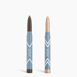 Two blue PrimePrometics™ Complete Eye Sticks Kit makeup sticks stand upright against a white background: the left is matte dark brown eyeshadow, and the right is a shimmery champagne eye brightener.