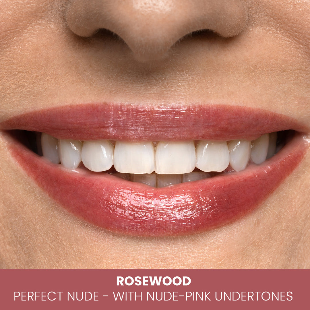 A close-up of a smiling mouth wearing glossy rosewood lipstick, described as the perfect nude with nude-pink undertones. The lips are well-defined, and teeth are visible.