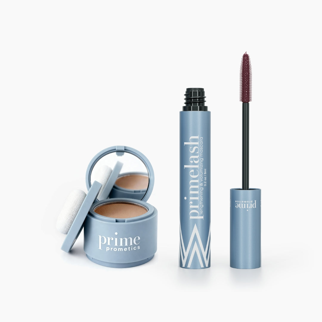 The PrimePrometics™ Beauty Essentials Set features a blue compact with Hairline Powder and mirror, plus an open blue PrimeLash Mascara tube with wand, labeled accordingly, all shown on a white background.