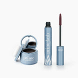 The PrimePrometics™ Beauty Essentials set features a light blue hairline powder compact with mirror and white puff beside a matching PrimeLash mascara tube with its exposed wand, all displayed against a clean white background.