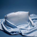 A light blue Makeup Bag by PrimePrometics™, crafted from elegant PU leather and featuring a convenient wrist strap, rests on matching blue satin fabric against a coordinating blue background—making it the ultimate beauty bag for any occasion.