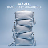 Four light blue PrimePrometics™ Makeup Bags with wrist straps are stacked atop one another against a blue background. Crafted from premium PU leather, these bags unite style and practical organization. The text above reads: BEAUTY, BEAUTIFULLY ORGANISED.