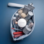 A top-down view of an open PrimePrometics™ Makeup Bag, crafted from sleek PU leather, filled with various silver cosmetics containers, Prime Prometics makeup brushes, and lipsticks on a blue surface.