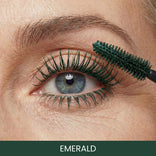 A close-up of a blue eye with emerald green mascara being applied to the upper lashes. The word EMERALD is written at the bottom of the image.