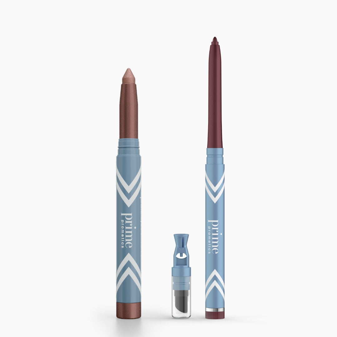 Two blue PrimePrometics™ Eye Lift Duo pencils stand upright—one with a metallic brown tip, the other maroon. In front sits a small sharpener with a clear cover.