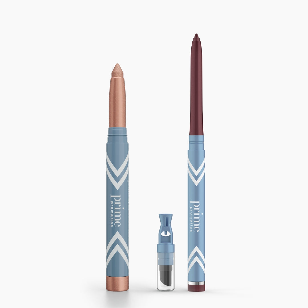 Two blue PrimePrometics™ Eye Lift Duo pencils with white chevrons stand upright: a thick, shimmery beige crayon and a slim, dark red eyeliner for women over 50. A small sharpener is placed in front of them. Both pencils are water-resistant.