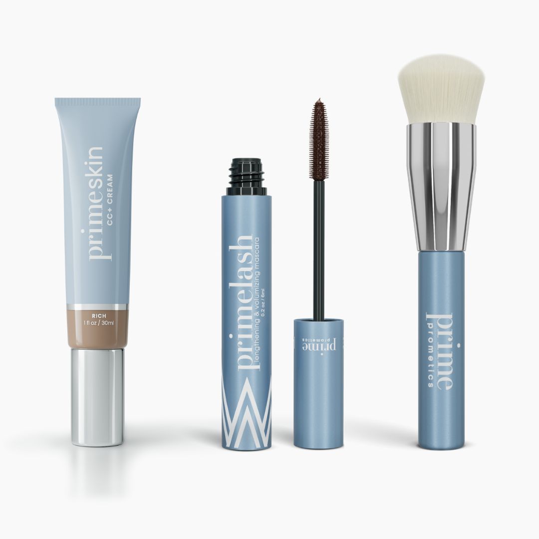 Four PrimePrometics™ Effortless Beauty Complete Bundle products—CC+ Cream, open Mascara with wand, and Foundation Brush with white bristles—stand upright in light blue packaging against a white background.