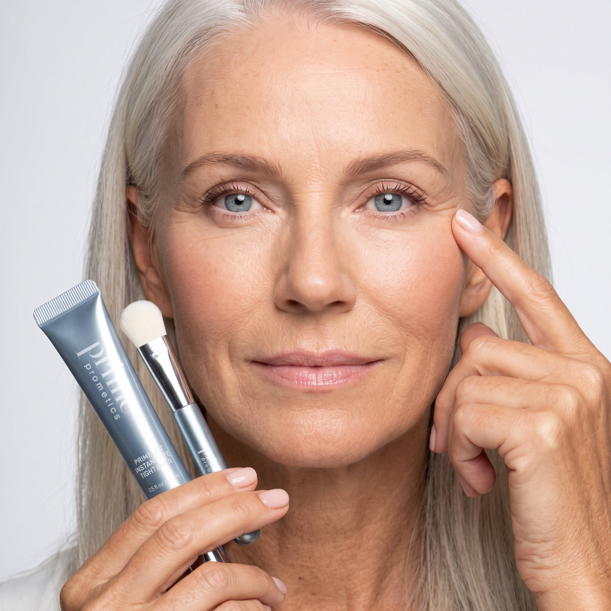 A woman uses a PrimeLift Precision Applicator Brush to apply PrimeLift Instant Eye Tightener while gently touching the skin under her eye.
