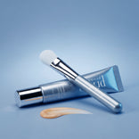 An ultra-soft PrimeLift Precision Applicator Brush rests on a tube of PrimeLift Instant Eye Tightener with a dollop of cream beside it.