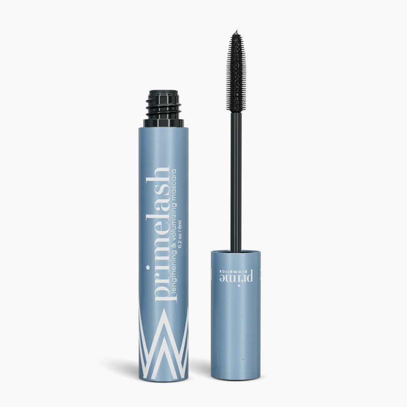 A blue tube of mascara labeled primelash stands upright with its wand applicator removed and placed beside it, showing the bristled brush. The background is white.