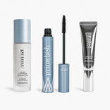 The PrimePrometics™ Prime Perfection Trio—featuring the Color Changing Foundation, PrimeLash Mascara (shown with the wand exposed), and Airbrushed Skin Primer—stands upright in sleek blue and silver packaging against a white background.
