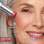 Eine lächelnde Frau trägt den PrimePrometics™ PrimeWands 5-in-1-Make-up-Stift in einem cremefarbenen Nude-Rouge-Ton auf ihre Wangen auf. Die Gebrauchsanweisung lautet: WANGEN: Auf den Wangen verblenden, um einen sanften, natürlich wirkenden, in der Intensität variierbaren Farbtupfer zu erzielen. LIPPEN: Auftragen, um einen gepflegten, rosigen Nude-Farbton für den Alltag zu erzielen.
