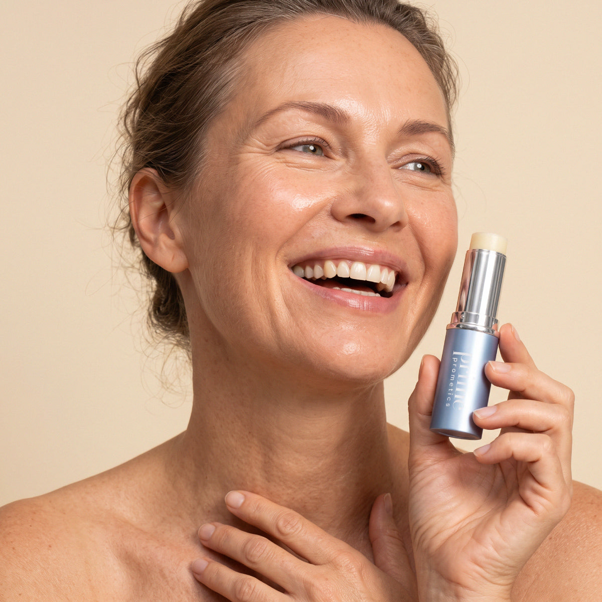 Eine lächelnde Frau mit strahlender, reifer Haut hält „PrimeWand Nourish“ von PrimePrometics™ nahe an ihr Gesicht; ihre Hand ruht sanft auf ihrer Brust vor einem hellbeigen Hintergrund und unterstreicht so die strahlende Schönheit von Frauen über 50.
