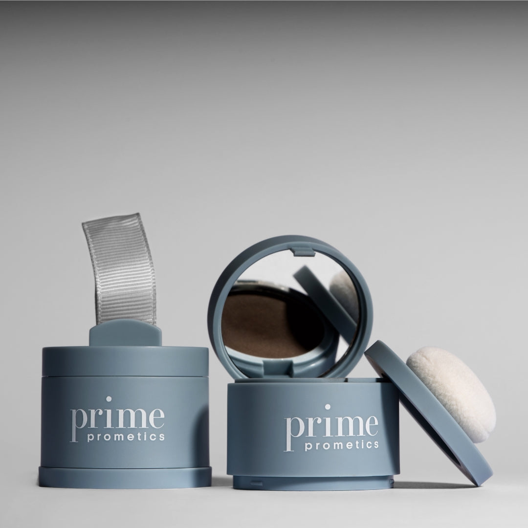 Three blue containers labeled prime prometics, one with a ribbon handle, one open showing a mirror and powder, and one with a white powder puff resting on top, against a neutral background.