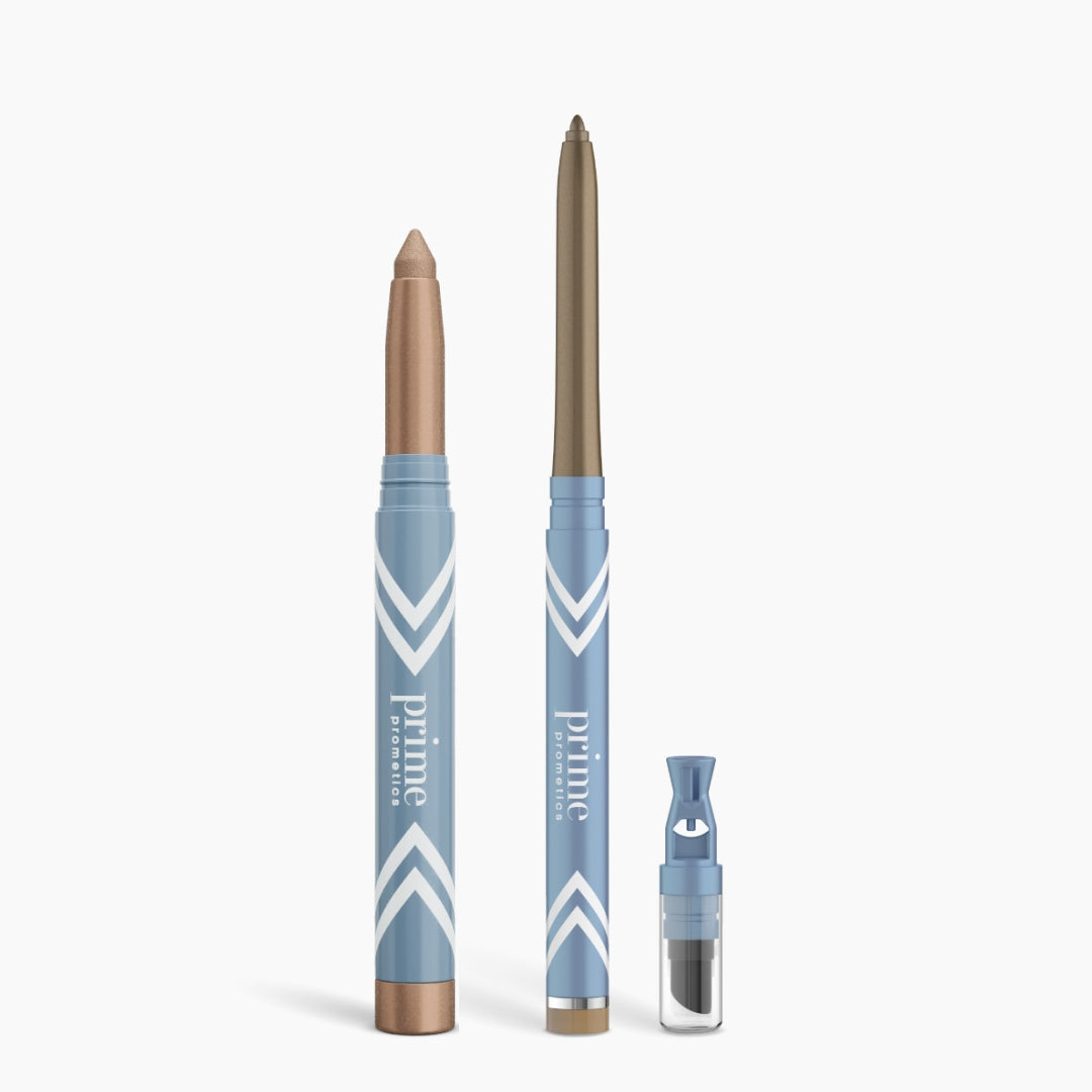 Three blue and copper PrimePrometics™ Eye Lift Duo makeup products—a thick eyeshadow stick, a slim eyeliner for women over 50, and a small clear powder container—are shown on a white background.