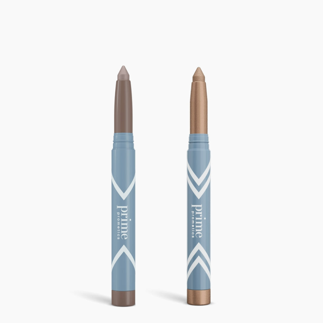 Two blue PrimePrometics™ Complete Eye Sticks Kit—one with a taupe tip, one with a shimmery bronze—stand upright on white, ideal for matte eyeshadow looks or an eye-brightening effect.