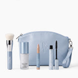 The PrimePrometics™ Prime Mini Essentials Travel Kit features a light blue makeup bag with a brush, primer spray, concealer stick, mascara, mini foundation, and eyeliner—each in matching sleek blue packaging—creating the perfect set of beauty essentials for travel, beautifully arranged on a white background.