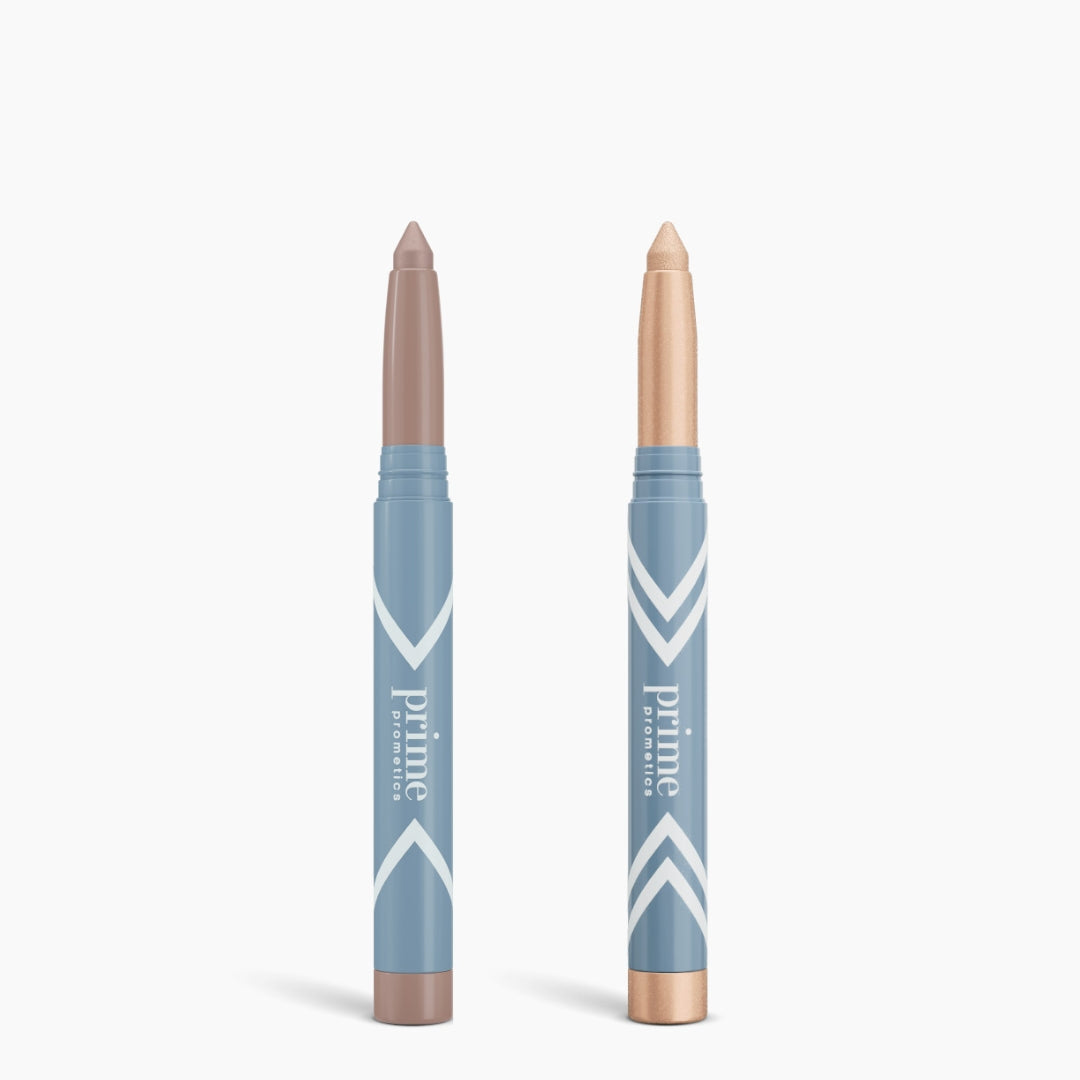 Two blue PrimePrometics™ Complete Eye Sticks Kit products stand upright on a white background. The left stick has a taupe matte eyeshadow tip, while the right displays a shimmery champagne eye brightener tip.