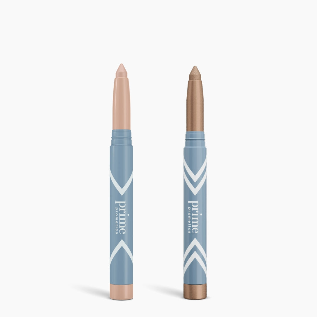 Two blue Complete Eye Sticks Kit tubes by PrimePrometics™ stand upright on a white background; each has a twist-up cream tip—light beige on the left for brightening, metallic bronze on the right for matte eyeshadow.
