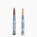 Two blue PrimePrometics™ Complete Eye Sticks Kit tubes stand upright. The left offers mauve matte eyeshadow; the right is a shimmery champagne eye brightener. Both feature twist-up packaging and white chevron patterns.